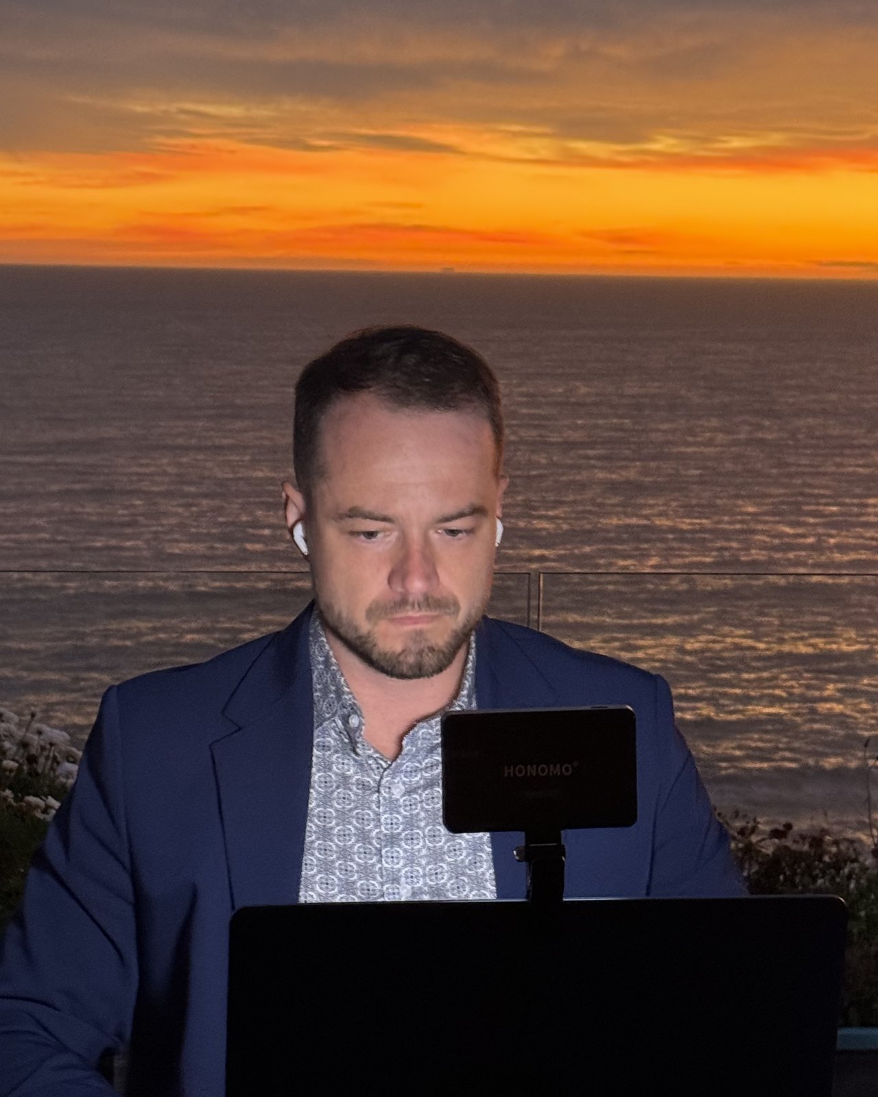 Blake on a sales call at sunset, laptop open, the Pacific behind him